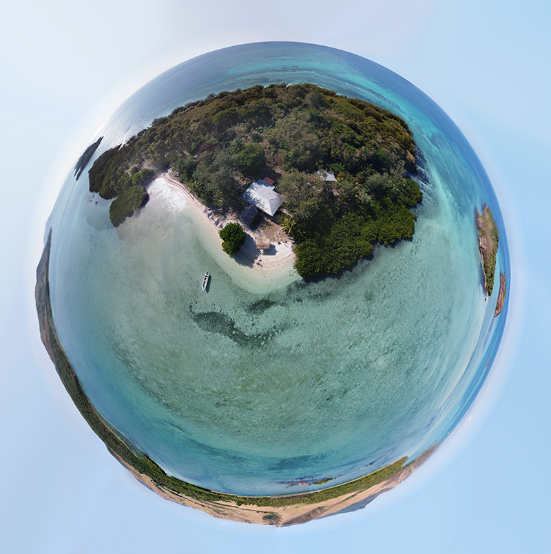 Fisheye camera view of a small island surrounded by crystal blue waters.