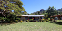 A one-story house in Marou Village Fiji with the mountain rising in the background and a large shade tree to the left.