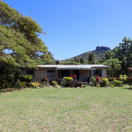 A one-story house in Marou Village Fiji with the mountain rising in the background and a large shade tree to the left.