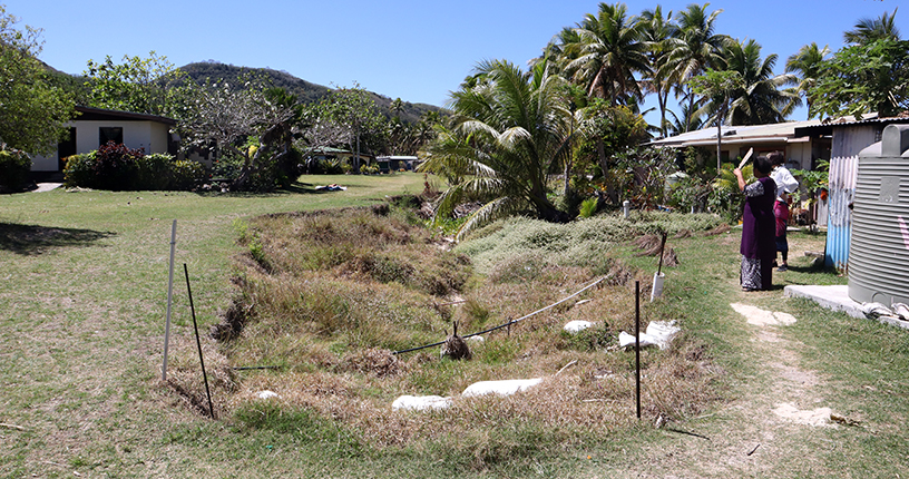 Land depression in the middle of the village surrounded by houses and trees.