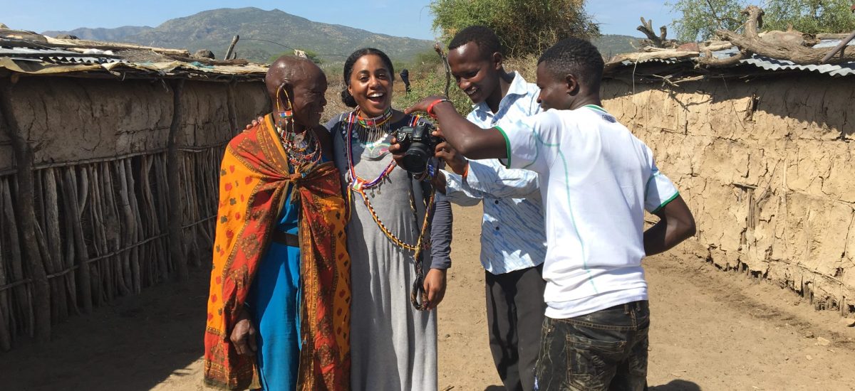 Tereneh Tereneh Idia, artist and founder of Idia'Dega, with residents of Olorgesailie. They are looking at a photo that had been taken earlier.