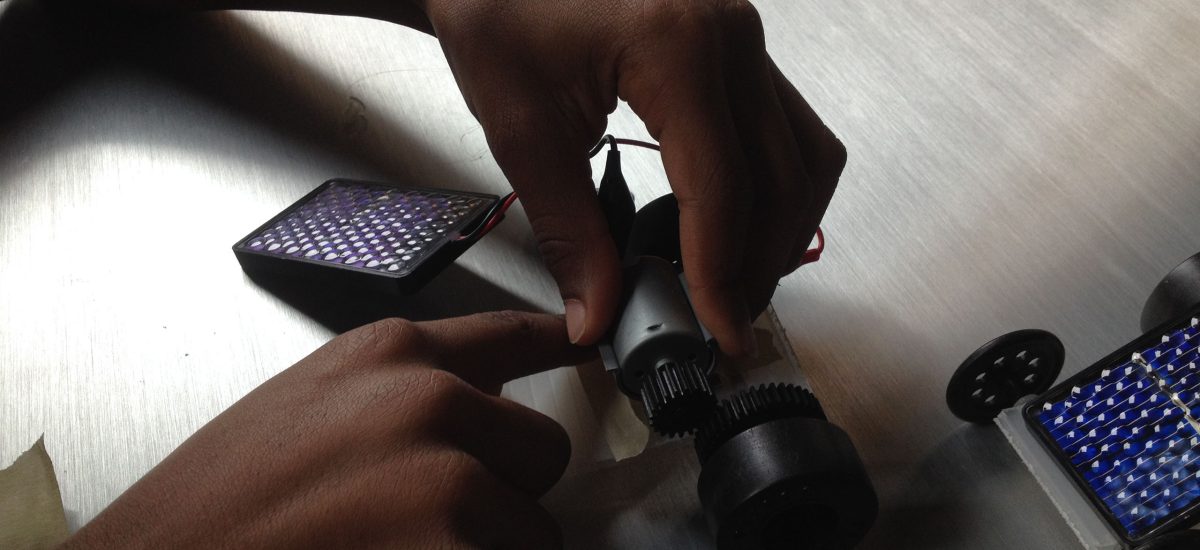 day5_2806 Youth tinker with solar technology during the 2015 Art+Energy Camp. In this photo we can see two hands adjusting the motor on a solar powered toy car.