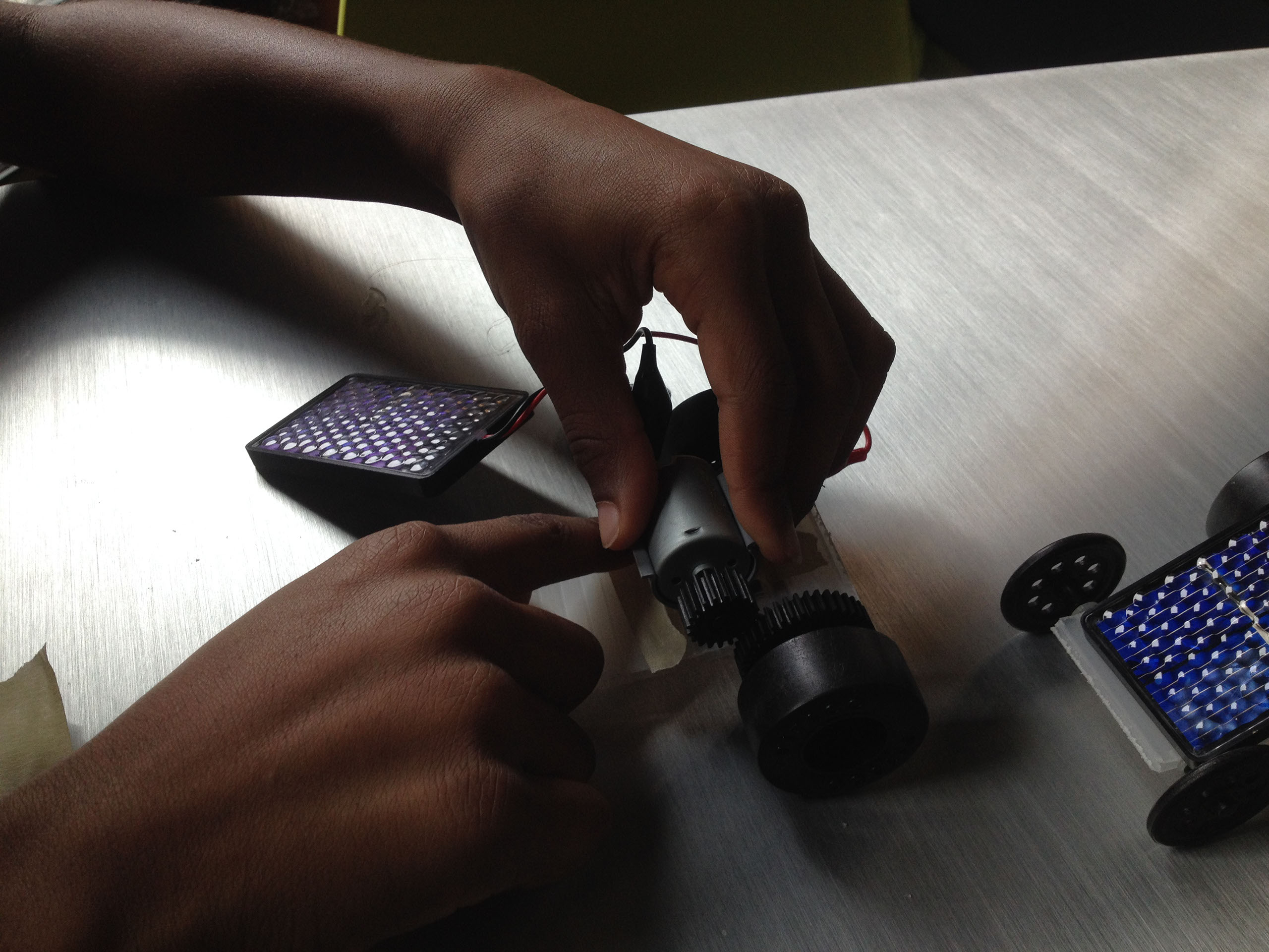 Youth tinker with solar technology during the 2015 Art+Energy Camp. In this photo we can see two hands adjusting the motor on a solar powered toy car.