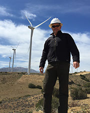 Photo of Todd Bartholf standing in the foreground with large on-shore wind turbines in the background.